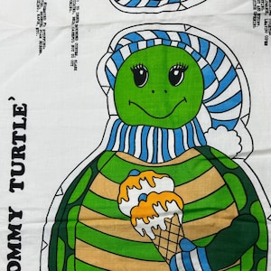 May include: A green and brown turtle wearing a blue and white striped hat and scarf, holding a cone of ice cream. The turtle is wearing yellow boots and the text 'TOMMY TURTLE' is written on the fabric.