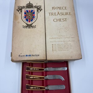 May include: A vintage 19-piece Sheffield English Stainless Steel Treasure Chest set. The box is beige with text and a crest. Inside, a red tray holds knives with brown and cream handles.