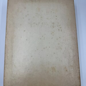 May include: A rectangular, off-white book with a worn appearance. The cover shows signs of age with brown spots and discoloration, suggesting it is vintage or antique. The edges are slightly worn.