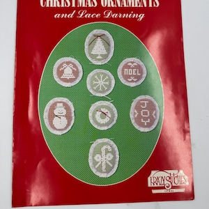 Può includere: Un libro di artigianato vintage intitolato "CHRISTMAS ORNAMENTS and Lace Darning" con una copertina rossa. La copertina presenta un cerchio verde con disegni di ornamenti natalizi ricamati. Gli ornamenti includono un albero di Natale, una campana, un fiocco di neve e un pupazzo di neve.