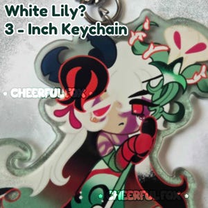 May include: A 3-inch acrylic keychain featuring a stylized character illustration with white hair, red eyes, and green and red accents. The text White Lily? 3-Inch Keychain and Cheerful Fox is printed on the surface. The design includes floral elements.