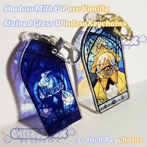 May include: Two stained glass window keychains, one blue and one yellow, with silver clasps. The keychains are 3 inches in length and feature a cartoon character design. Text on the keychains reads "Shadow Milk & Pure Vanilla" and "Stained Glass Window Keychains."
