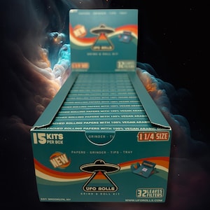 Op de afbeelding: Een doos met 15 UFO Rolls Grind & Roll Kits. Elke kit bevat 1 1/4 formaat rolpapier, een grinder, tips en een dienblad. De doos is turquoise en heeft een UFO-afbeelding en de tekst "UFO Rolls Grind & Roll Kit".