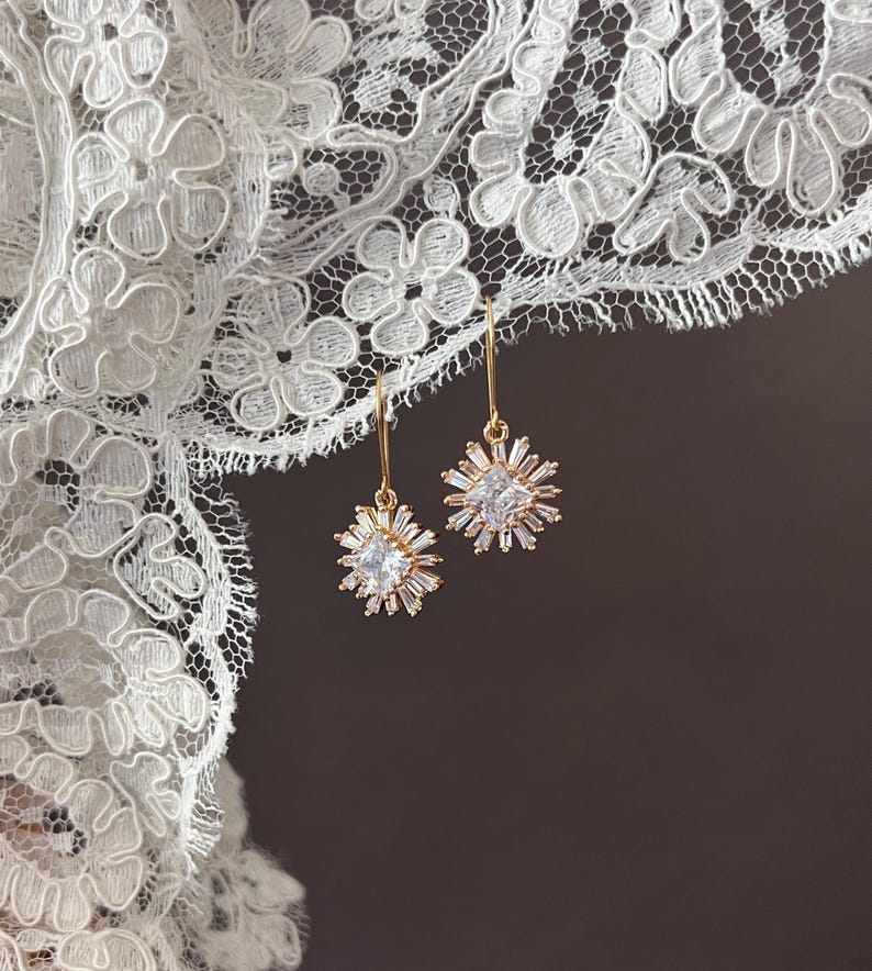May include: A pair of gold earrings with a starburst design featuring clear cubic zirconia stones.