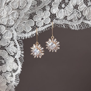 May include: A pair of gold earrings with a square-shaped clear crystal surrounded by smaller crystals in a starburst design.