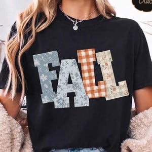 Könnte beinhalten: Ein schwarzes kurzärmeliges T-Shirt mit dem Wort FALL auf der Brust. Jeder Buchstabe hat ein eigenes Muster: Das F und A haben einen blauen Blumenaufdruck, das L ein orange-weißes Vichy-Karo und das letzte L ein kariertes Design.