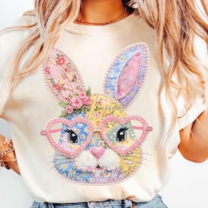 May include: Cream-colored t-shirt featuring a colorful patchwork bunny design. The bunny wears heart-shaped glasses and has floral accents. The text "Summer Designs" is visible. The design is embellished with pearls.