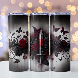 Puede incluir: Tres vasos de acero inoxidable con un diseño gótico. El diseño presenta rosas negras y rojas, mariposas y una jeringa llena de líquido rojo. El fondo es un degradado de blanco y negro.