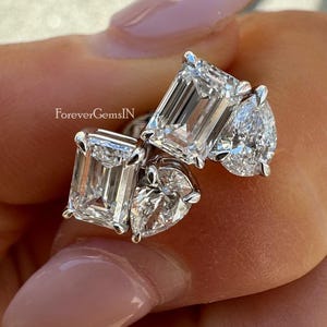 Puede incluir: Colección de cuatro anillos de diamantes con diferentes cortes: esmeralda, pera y corazón. Los anillos están engarzados en una banda plateada. Los anillos brillan y reflejan la luz. Fondo neutro.