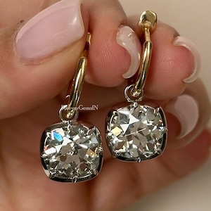 Peut inclure: Une paire de boucles d'oreilles créoles en or avec une grande pierre précieuse carrée transparente suspendue à chaque créole.