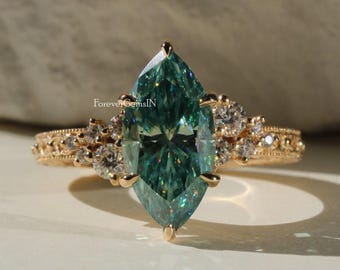 May include: A gold ring featuring a marquise-cut teal gemstone as the centerpiece. The band is adorned with small, round accent stones and intricate detailing. The ring is set against a neutral background, highlighting its elegant design.