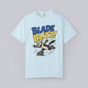 May include: Light blue t-shirt featuring a cartoon ferret on roller skates with the words "BLADE BLITZ!" in blue and yellow. The ferret has a brown and white body and is wearing blue roller skates.