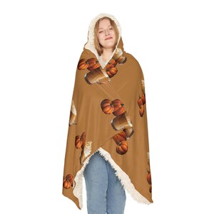 Puede incluir: Una manta con capucha en un tono marr&oacute;n c&aacute;lido, adornada con un patr&oacute;n repetido de calabazas y bebidas de caf&eacute;. El interior de la capucha y el ribete presentan un suave forro de sherpa color crema. La manta est&aacute; dise&ntilde;ada para la comodidad.
