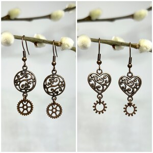 May include: Two pairs of bronze earrings with a filigree design. One pair features a round filigree charm with a gear charm dangling below. The other pair features a heart-shaped filigree charm with a gear charm dangling below.