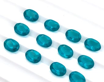 May include: Ten oval-shaped turquoise gemstones on a white surface. The gemstones are smooth and have a slight sparkle.
