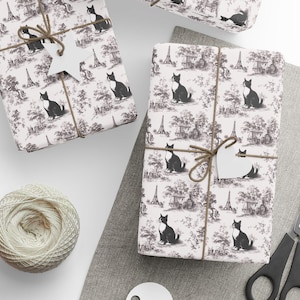 Op de afbeelding: Cadeaus verpakt met een zwart-wit katten-toile-patroon. Elk pakket is vastgebonden met touw en een blanco label. Een kluwen touw, een schaar en blanco labels zijn ook zichtbaar.
