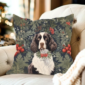 May include: A square throw pillow featuring a brown and white spaniel dog centered against a dark background with a botanical pattern of green pine needles, leaves, and clusters of bright red berries surrounding the animal portrait.
