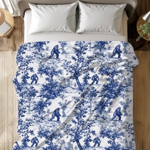 Puede incluir: Una funda nórdica blanca con un patrón toile azul y blanco que presenta un diseño repetitivo de un gran simio caminando por un bosque.