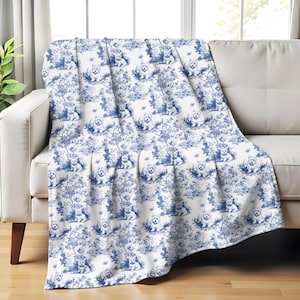 May include: A white throw blanket with a blue and white toile pattern featuring a repeating design of small dogs in a garden setting.