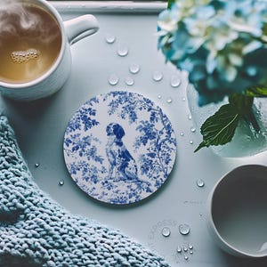 Peut inclure: Un dessous de verre en c&eacute;ramique blanche avec un motif floral bleu et blanc repr&eacute;sentant un chien. Le dessous de verre est rond et poss&egrave;de un bord sur&eacute;lev&eacute;.