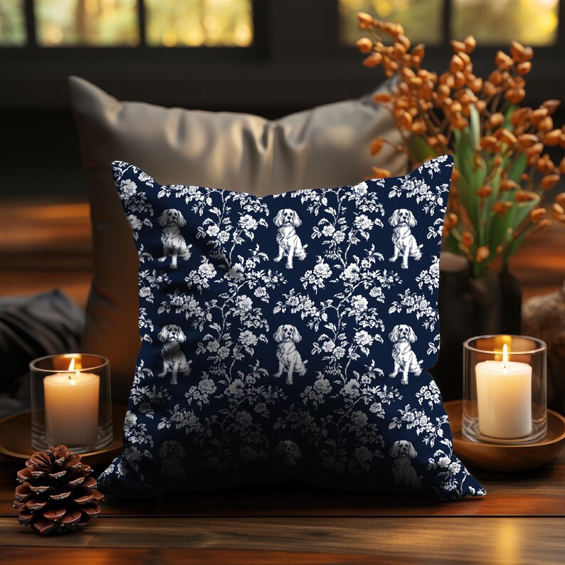 May include: Square navy blue throw pillow with a white floral and dog pattern. The pillow features a repeating design of Cavalier King Charles Spaniels among white flowers and foliage. The pillow is placed on a wooden surface.