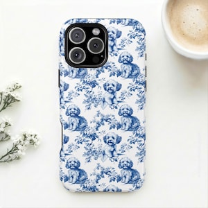 Könnte beinhalten: Eine weiße Handyhülle mit einem blauen Toile-de-Jouy-Muster, das kleine Hunde und florale Elemente zeigt. Die Hülle hat eine glänzende Oberfläche und ein schwarzes Kameramodul.