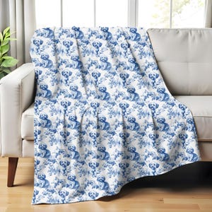 May include: A white throw blanket with a blue and white pattern of small dogs. The dogs are sitting in a floral design.