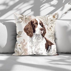 Puede incluir: Una almohada con un perro blanco y marrón con orejas caídas. El perro está rodeado de un patrón floral con hojas y flores blancas y marrones.