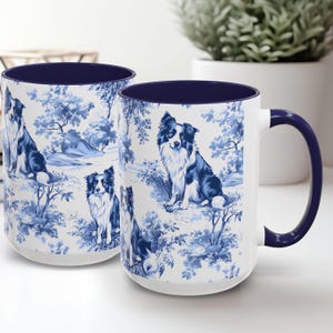 May include: Two white ceramic mugs with blue and white patterned design featuring border collies. The mugs have a navy blue rim and handle.