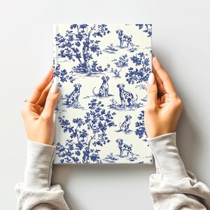 May include: A white notebook cover with a blue and white toile pattern featuring dalmatian dogs. The pattern includes stylized trees and flowers.