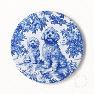 May include: Two white dogs with curly fur are sitting on a blue and white patterned background. The dogs are in a toile pattern, a traditional French design.