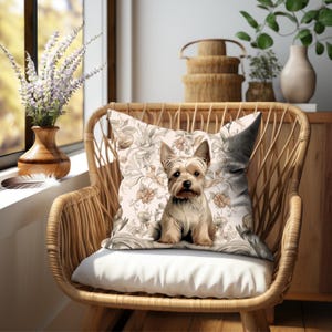 Puede incluir: Una almohada decorativa con un patr&oacute;n floral y una ilustraci&oacute;n de un perro Yorkshire Terrier. La almohada es beige con detalles marrones y est&aacute; sentada en una silla de mimbre.