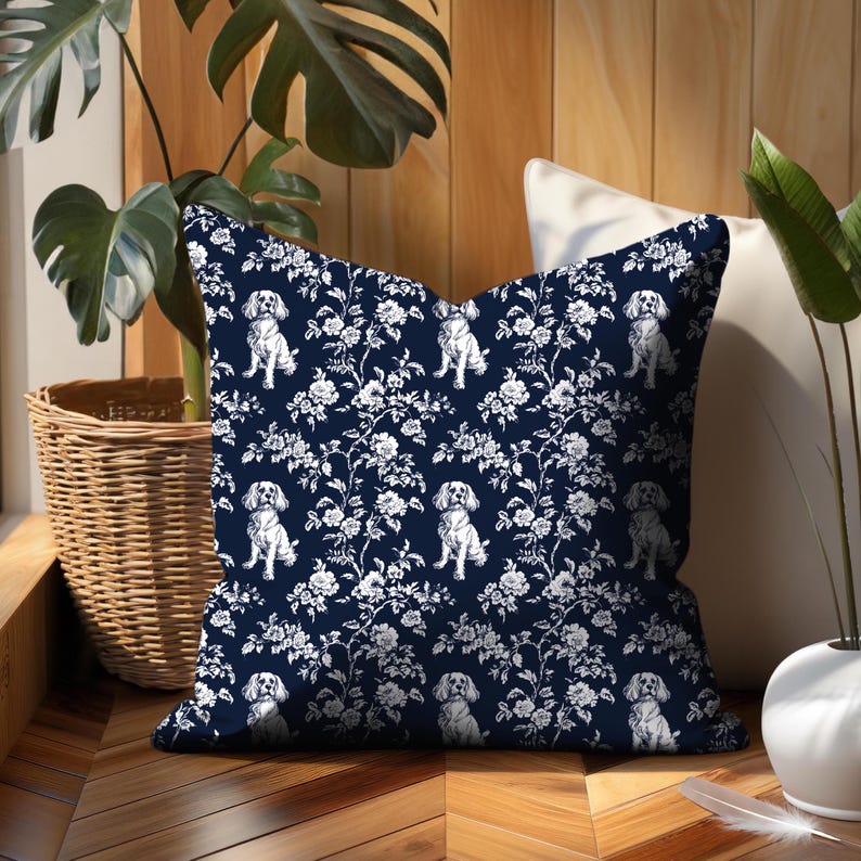 May include: A navy blue throw pillow with a white floral and dog pattern. The pillow features a repeating design of white flowers and Cavalier King Charles Spaniels. The pillow is square and appears to be made of a soft fabric.