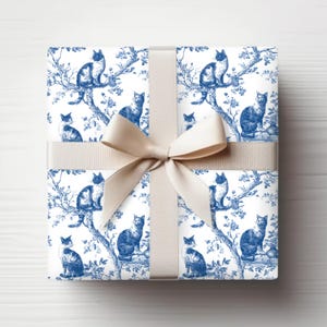 May include: A wrapped gift with a cream-colored ribbon. The wrapping paper features a blue and white toile pattern of cats perched on tree branches. The bow is tied in a classic style, creating a decorative presentation.