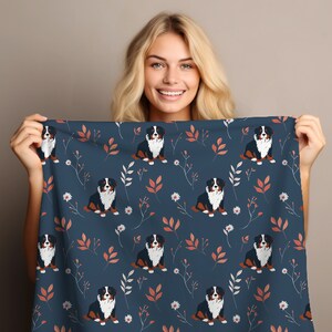 Op de afbeelding: Een blauwe stof met een herhalend patroon van Berner Sennenhonden, bladeren en bloemen. De honden zijn zwart, bruin en wit. De bladeren zijn roodbruin. De bloemen zijn wit.