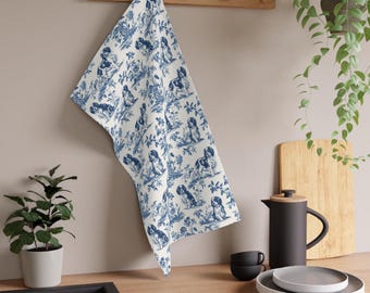 Könnte beinhalten: Ein weißes Küchentuch mit einem sich wiederholenden blauen Toile-Muster aus Hunden und floralen Elementen. Der Stoff hängt über einer hölzernen Wandleiste und zeigt einen detaillierten Illustrationsstil mit verschiedenen Hundeposen.