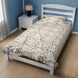 Pode incluir: Um edredom branco de tamanho twin com fundo creme e um padr&atilde;o repetido de c&atilde;es brancos e flores laranja. O edredom est&aacute; em uma estrutura de cama branca com uma cabeceira branca.