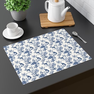 May include: A white placemat with a repeating pattern of blue dogs and trees. The placemat is on a black surface.