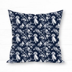 May include: Square throw pillow with a navy blue background and a white floral and dog pattern. The design features repeating images of dogs and floral elements, creating a decorative and stylish look. The pillow is a square shape.