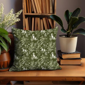 May include: A green throw pillow with a white floral pattern and a repeating image of a dog. The pillow is sitting on a wooden table.