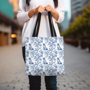 May include: A white tote bag with a blue and white pattern of dogs and floral designs. The bag has black handles.
