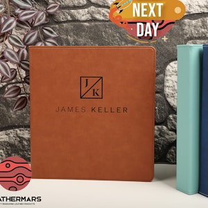 May include: A brown leather folder with a personalized monogram of "J/K" and the name "JAMES KELLER" embossed in black. The folder is on a brick wall background.