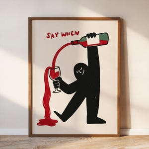 May include: A framed wall art print featuring a black silhouette figure pouring red liquid from a bottle into a wine glass. The text SAY WHEN is printed in red above the figure. The liquid overflows from the glass onto the bottom surface.