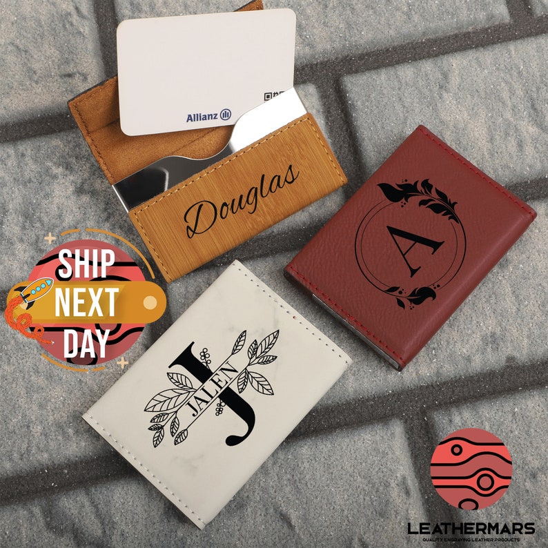 May include: Three personalized leather card holders with different designs. The first is brown with the name "Douglas" engraved on it. The second is red with a floral design and the letter "A" in the center. The third is white with a marble pattern and the letter "J" with the name "Jalen" engraved on it.