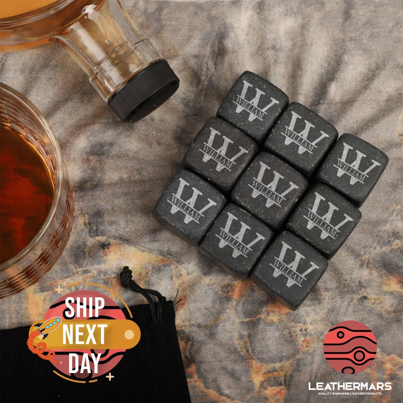 May include: Set of nine black stone whiskey chilling cubes with the name "William" engraved on each cube. The cubes are arranged in a square shape and are displayed on a textured surface.
