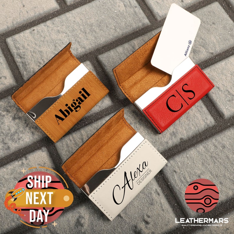 May include: Three personalized leather business card holders. One is brown with the name Abigail engraved on it. Another is red with the initials CS engraved on it. The third is white with the name Alexa Designer engraved on it.