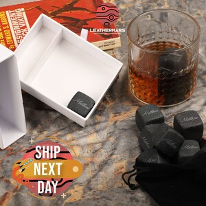 May include: A set of six black personalized whiskey stones in a black velvet pouch. The stones are engraved with the name "Matthew".