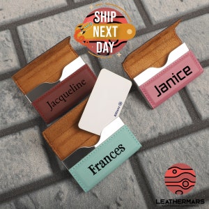 May include: Three personalized leather business card holders in different colors: burgundy, pink, and light blue. Each holder has a silver metal insert and a name engraved on the front. The names are Jacqueline, Janice, and Frances.