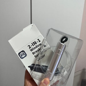 May include: A silver 2-in-1 window breaker and seatbelt cutter tool in a clear plastic package. The package has a white label with the text "2-IN-1 Window Breaker & Seatbelt Cutter".