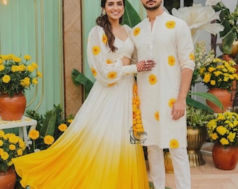 May include: A white and yellow ombre lehenga with long sleeves and sunflower prints, paired with a white kurta featuring matching sunflower prints and white trousers. The ensemble includes a yellow tassel accessory and a small logo reading Ethnic Outfits.